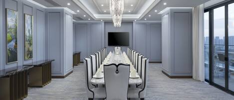 A conference room with a long table, chairs, a chandelier, a flat-screen TV, and a city view through large windows.