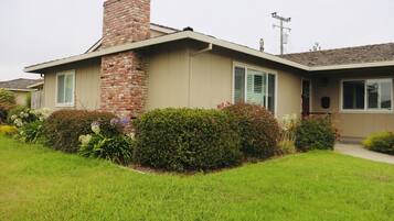 A single-story house with a brick chimney, beige siding, and green shutters.