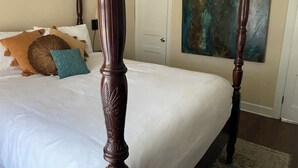 A four-poster bed with a white bedspread, multiple pillows in various colors, a door, and a painting on the wall. - Comfortable and Quiet 3 Bedroom Duplex (Nashville)