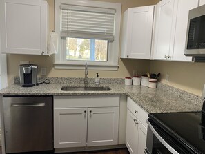 A kitchen with white cabinets, a granite countertop, a coffee maker, a sink, and a microwave.