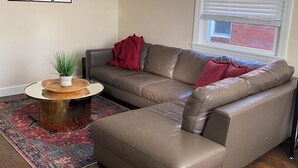 A living room with a sectional sofa, a round coffee table, a ceiling fan, and a window with blinds. - Comfortable and Quiet 3 Bedroom Duplex (Nashville)