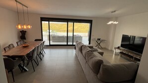 A modern living room with a large sofa, dining table, and TV. - Atico apartment with views of the Casares golf course, 3,00 metres from Finca Cortesin (Casares Costa Golf)