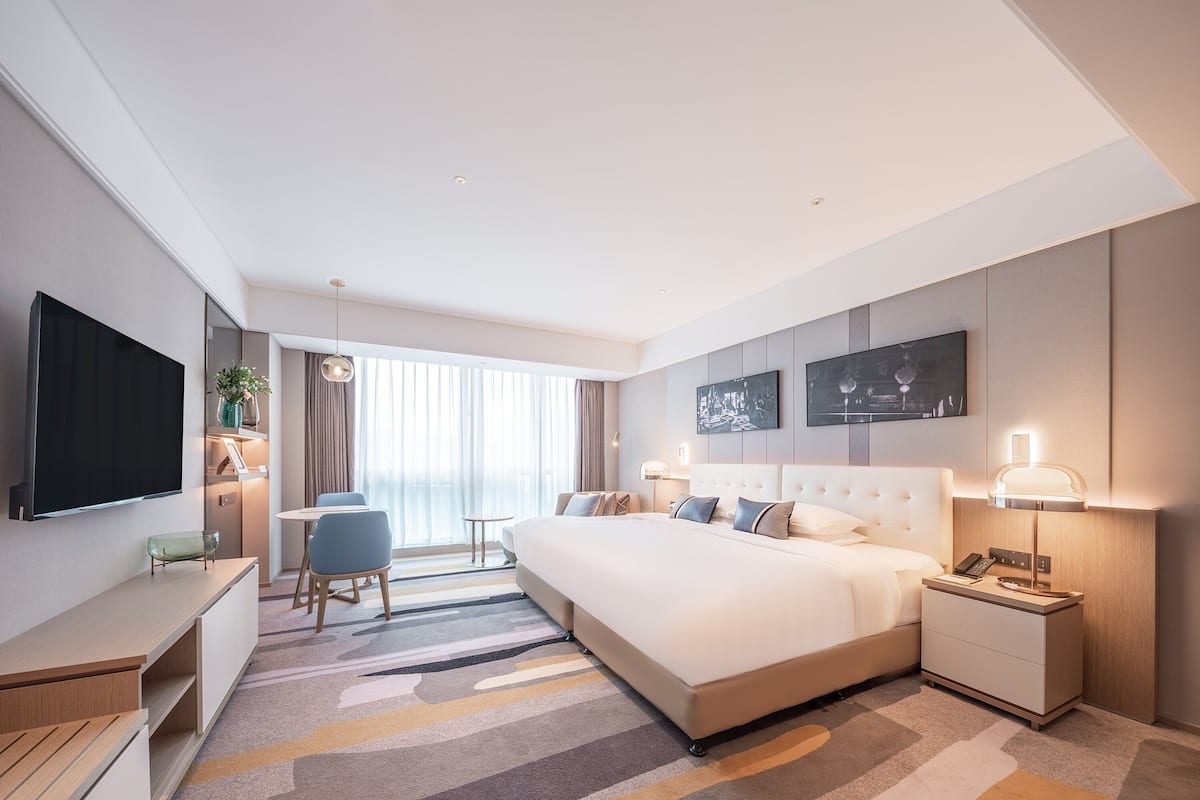 Une chambre d’hôtel moderne équipée d’un grand lit, de tables de chevet, d’un bureau, d’une chaise et d’un téléviseur.