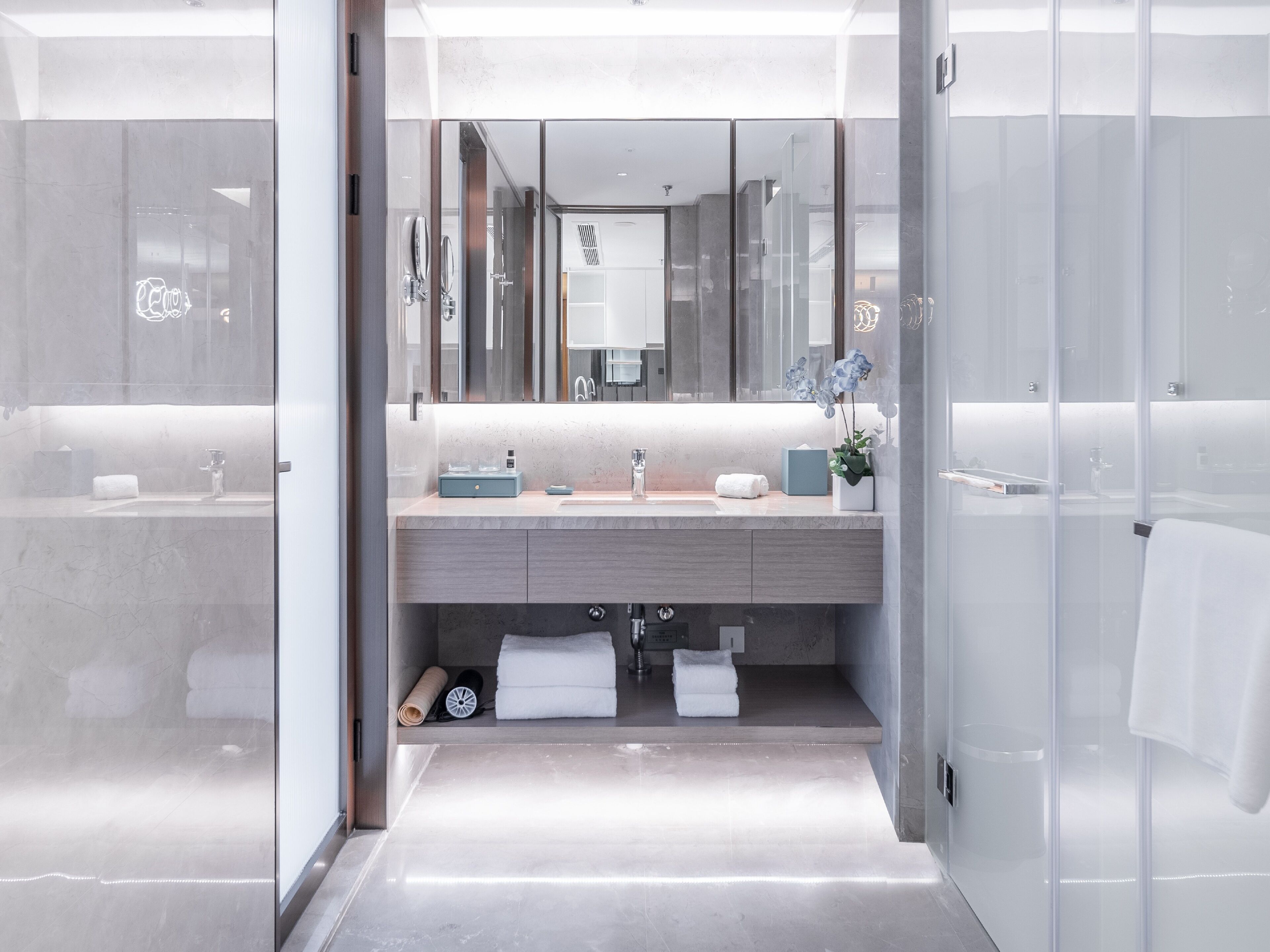 A modern bathroom with a glass shower enclosure, a marble countertop, and a large mirror.