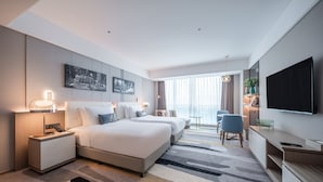 A modern hotel room with a large bed, bedside tables, a TV, and a seating area with a table and chairs.