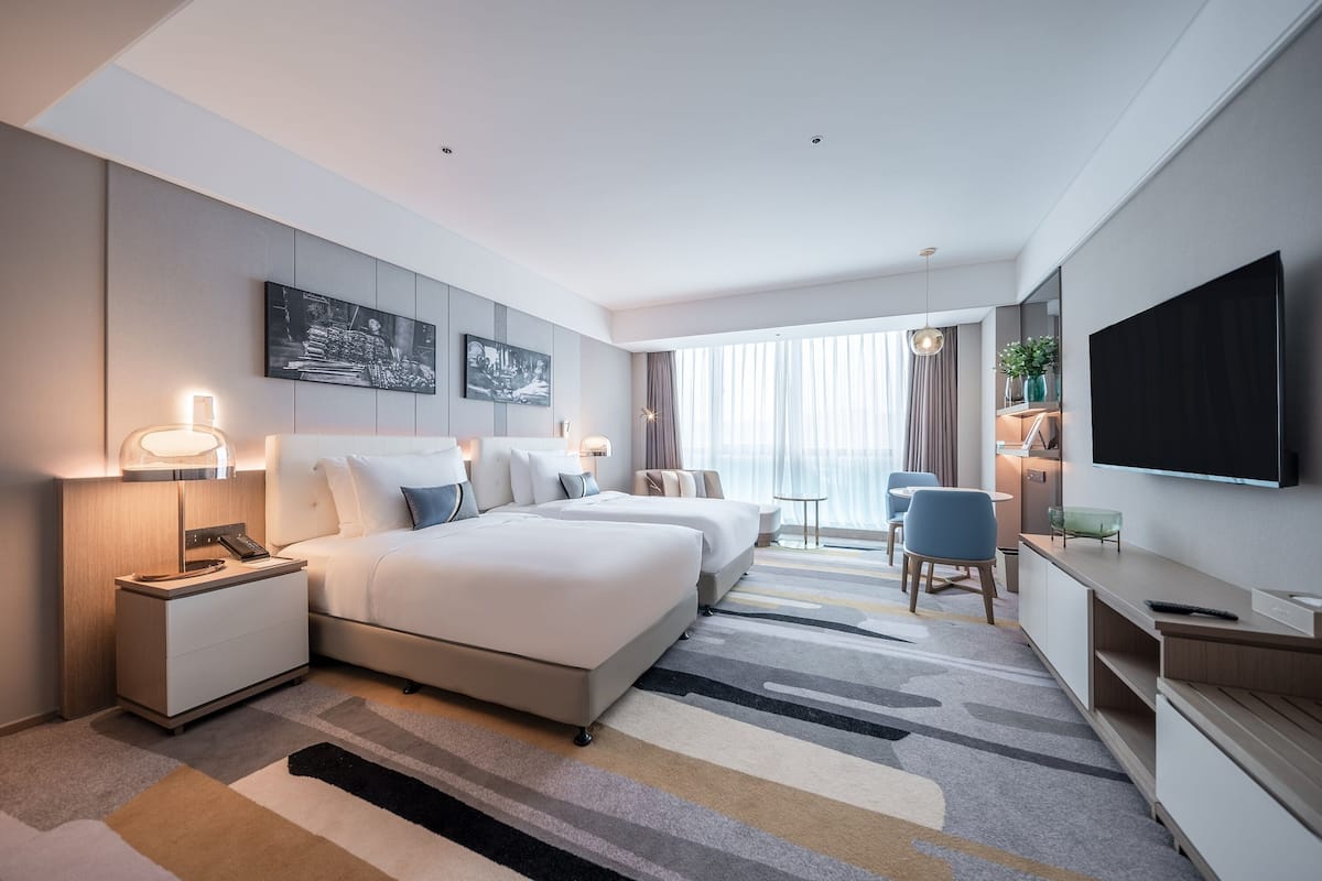 Une chambre d’hôtel moderne dotée d’un grand lit, de tables de chevet, d’une télévision et d’un coin salon avec une table et des chaises.