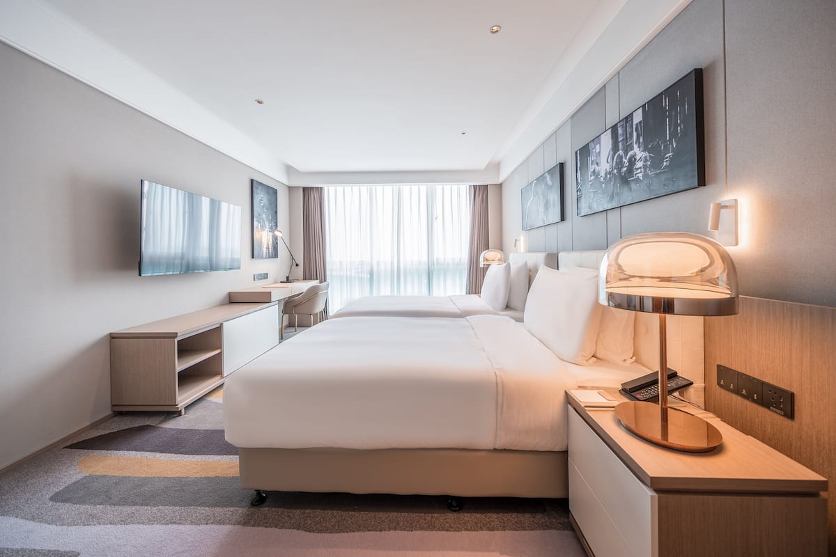Une chambre d’hôtel moderne dotée d’un grand lit, d’un bureau, d’une chaise, d’un téléviseur à écran plat et d’œuvres d’art accrochées aux murs.