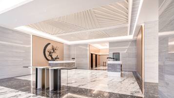 Een ruime lobby met een hoge plafond, marmeren vloeren en een centraal gelegen receptiebalie.