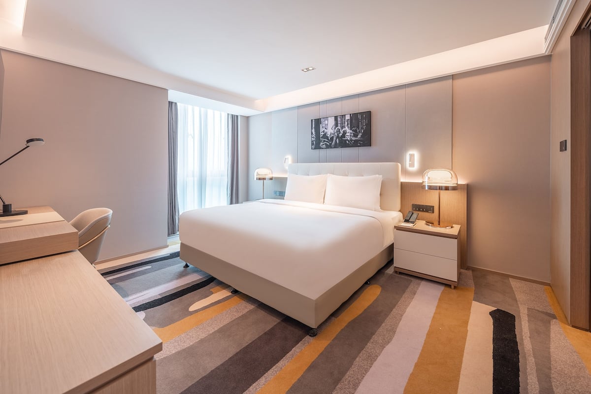 Une chambre d’hôtel moderne, dotée d’un grand lit, de tables de chevet, d’un bureau et d’une chaise.