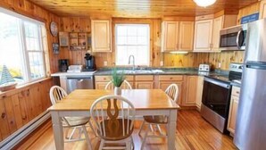 A wooden cabin kitchen with a dining table and chairs, a refrigerator, a stove, and a microwave. - Lakefront, 5 min to Colgate, Sleeps 6, Kayaks (Hamilton)