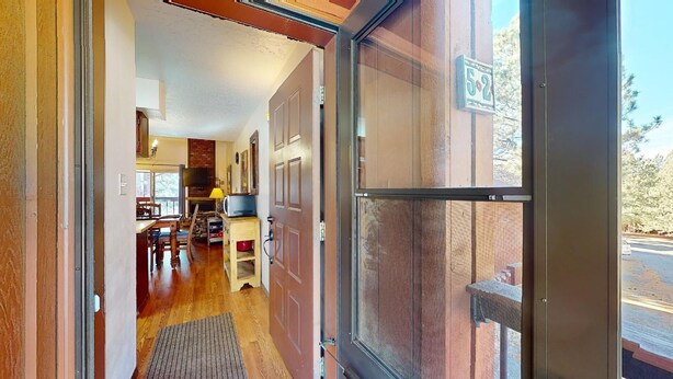 A hallway leading to a dining area with a fireplace, a television, and a door with a number plaque. - Pet Friendly | Close to Lifts | Fireplace | Charming | Angel Fire Chalet 52 (Angel Fire)
