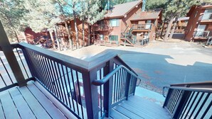 A wooden deck with a metal railing overlooking a street with buildings. - Pet Friendly | Close to Lifts | Fireplace | Charming | Angel Fire Chalet 52 (Angel Fire)