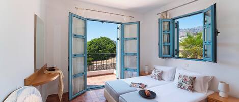 A bedroom with a bed, bedside tables, a desk, and a view of the outdoors.