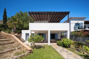 A modern two-story house with a covered patio, stone steps, and a garden.
