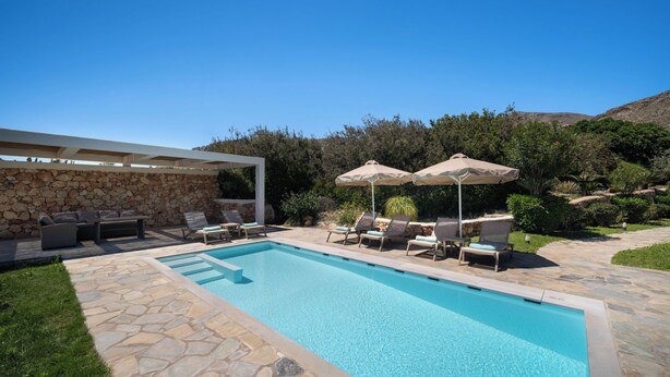 Une piscine entourée de murs de pierre et de verdure, avec des chaises longues et des parasols.