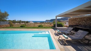 Une piscine avec une terrasse en pierre, des chaises longues et un mur en pierre.