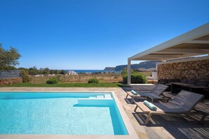 Una piscina con cubierta de piedra, sillas de descanso y un muro de piedra.