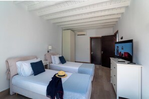 A hotel room with two beds, a TV, a wardrobe, and an air conditioning unit.