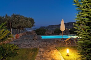 Une terrasse en pierre avec une piscine, des chaises longues et un chemin éclairé.
