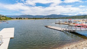 Ein See mit Booten, einer Anlegestelle und Bergen im Hintergrund.