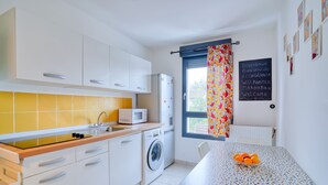 A modern kitchen with white cabinets, a washing machine, and a dining area with a table and chairs. - Chambres d'hôtes de Luxe Ma SuK (Saint-Denis)