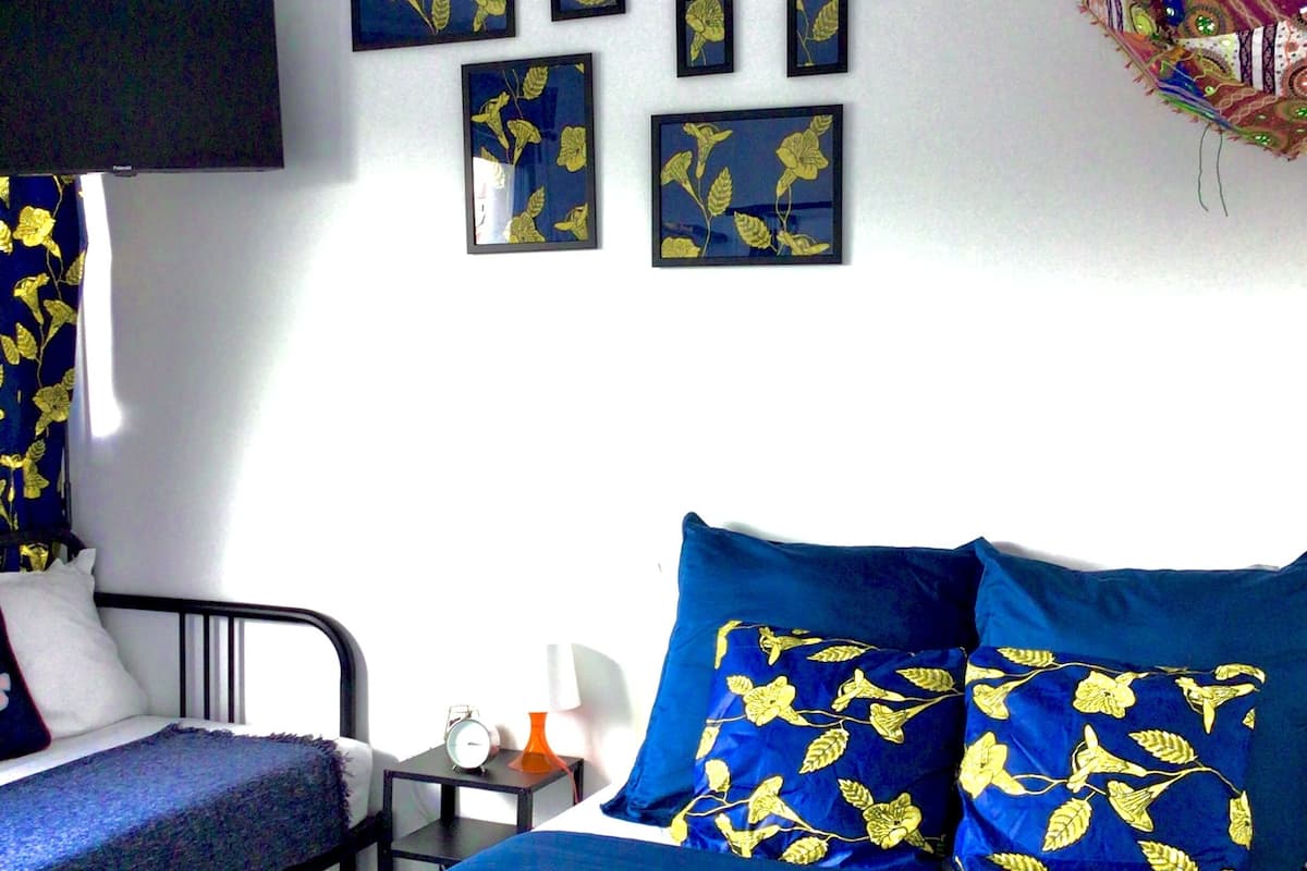 Une chambre à coucher avec un lit, deux oreillers, une table de chevet, une petite table et un téléviseur fixé au mur.