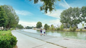 A paved walkway alongside a canal with trees and buildings in the background. - Chambres d'hôtes de Luxe Ma SuK (Saint-Denis)