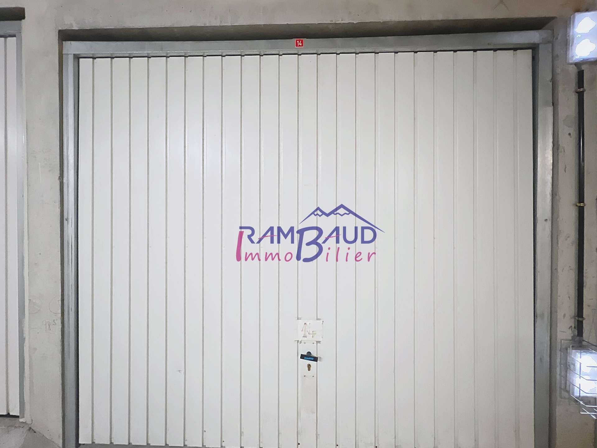 A closed metal garage door with the logo "RAMBAUD Immobilier" and a number "14" above it.