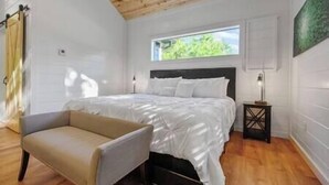 A bedroom with a bed, a chair, a nightstand, a window, and a wooden ceiling. - SERENITY NOW · Relax & Unwind (Broken Bow)
