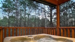 A hot tub with a wooden deck and a forest view. - SERENITY NOW · Relax & Unwind (Broken Bow)