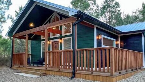 A cabin with a wooden deck, a covered porch, and a large window. - SERENITY NOW · Relax & Unwind (Broken Bow)