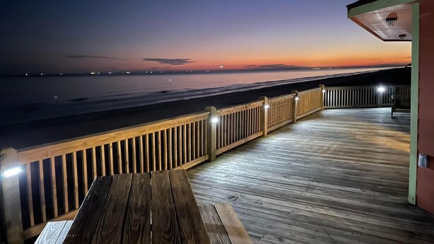 A wooden deck with a railing overlooking a beach at sunset. - Stunning Beachfront 3 Bedroom Home, CoralMoonBeach (Gilchrist)