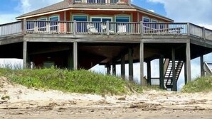 A beachfront house with a balcony, a staircase, and a sandy foreground. - Stunning Beachfront 3 Bedroom Home, CoralMoonBeach (Gilchrist)