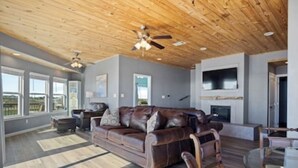 A spacious living room with a wooden ceiling, leather sofa, and a fireplace. - Stunning Beachfront 3 Bedroom Home, CoralMoonBeach (Gilchrist)