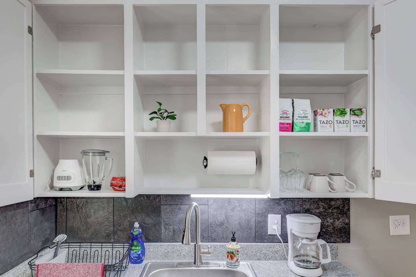 A kitchen with white cabinets, a sink, a coffee maker, and various kitchen items.
