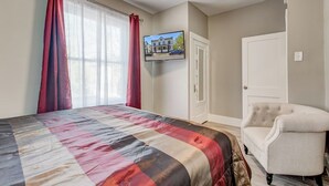 Une chambre à coucher avec un lit, une chaise, un téléviseur fixé au mur et une porte.