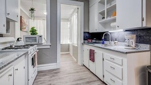 Une cuisine moderne avec des meubles blancs, un plan de travail en granit, une cuisinière à gaz, un four à micro-ondes et une machine à café.