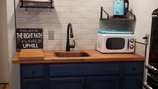 A kitchen with a wooden countertop, a sink, a microwave, and a coffee maker on a shelf.