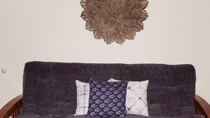 A dark grey sofa with two patterned cushions, a decorative wall piece, and wooden flooring.