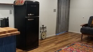 A compact living space with a kitchenette, a wooden floor, a colorful rug, a clock, and a grey curtain.