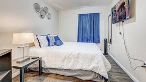 Una camera da letto con un letto, un comodino, una lampada, una TV a parete e una finestra con tende blu.