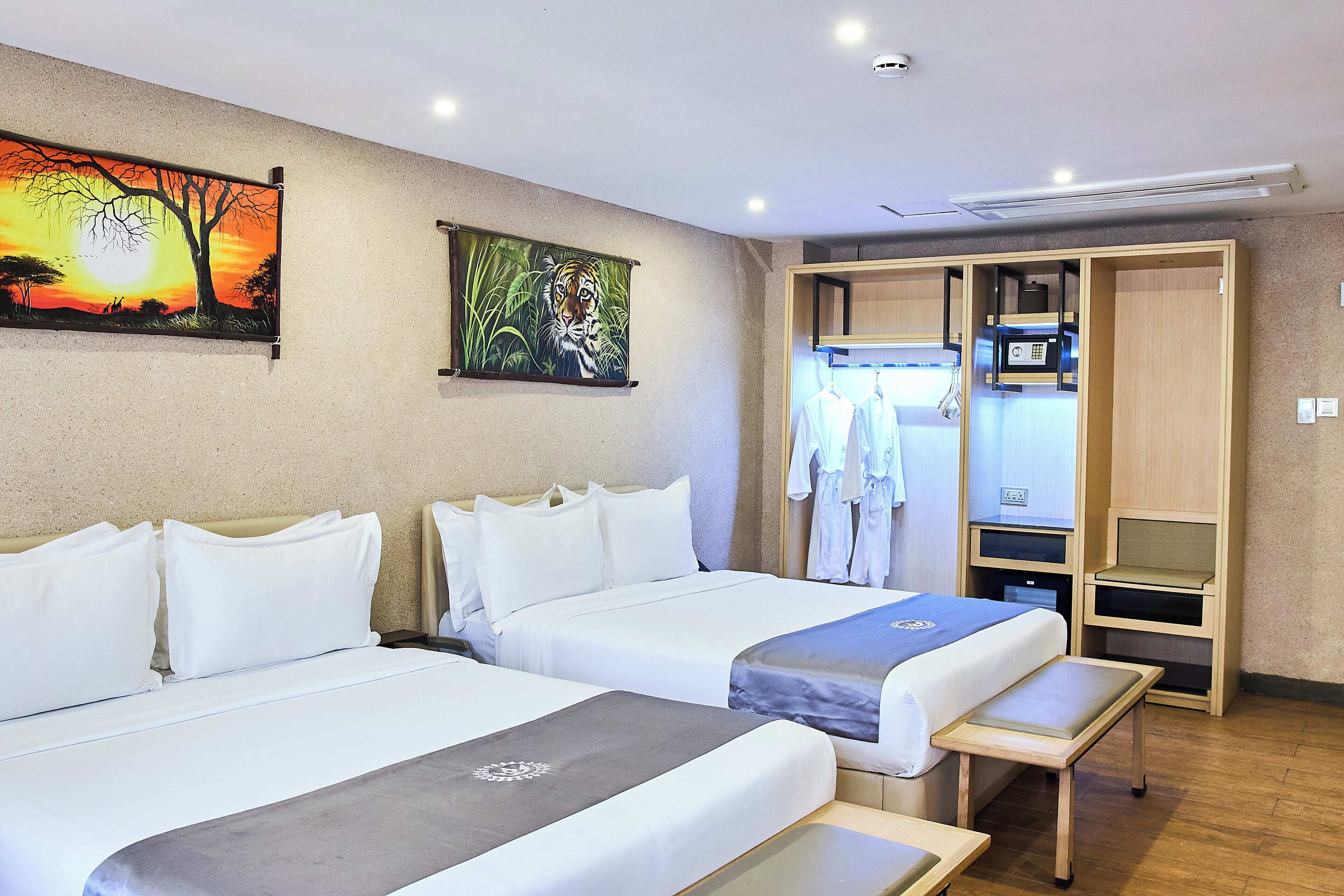 A hotel room with two beds, a wardrobe, a desk, and a painting on the wall.