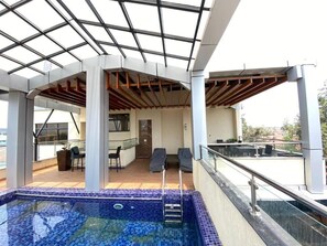 Una piscina interior con piso de baldosas, rodeada por una zona cubierta con sillas y una mesa.