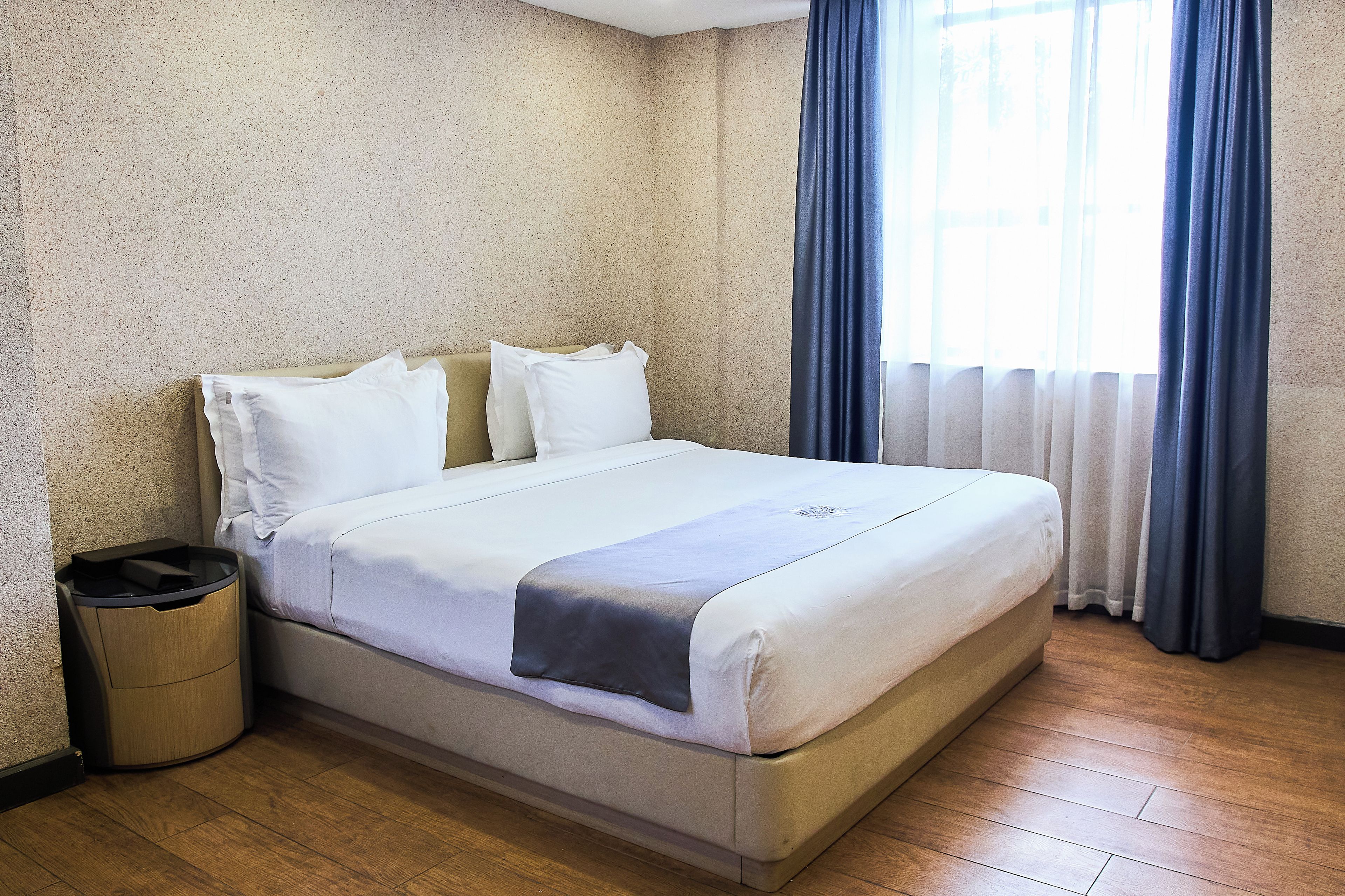 A hotel room with a bed, a trash bin, and a window with curtains.