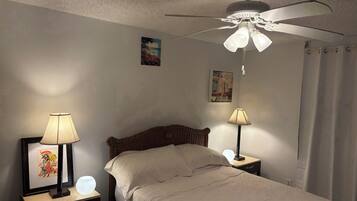 A bedroom with a bed, two bedside tables with lamps, a ceiling fan, and a painting on the wall.