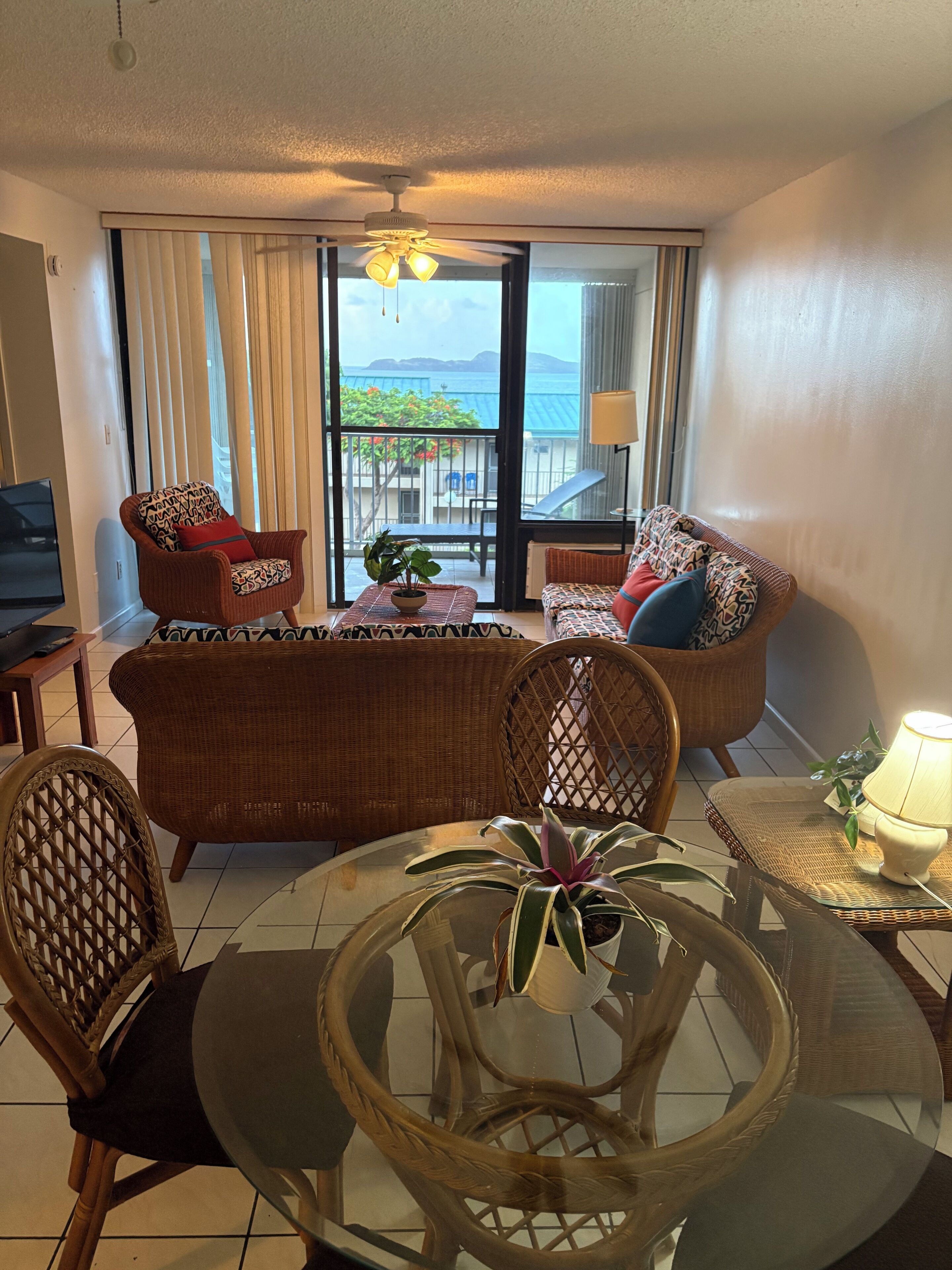 A living room with a sofa, chairs, a glass table, and a balcony with a view.