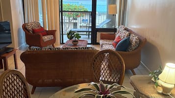 A living room with a sofa, chairs, a glass table, and a balcony with a view.