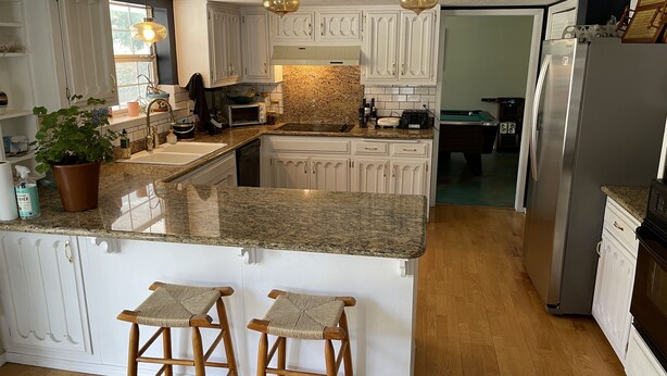 Une cuisine moderne avec des meubles blancs, des plans de travail en granit et un îlot central doté de tabourets de bar.