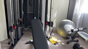 Une salle de sport à domicile équipée d’un banc de musculation, d’haltères, d’un ballon lesté et d’une barre de traction.