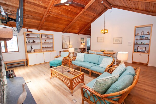 A spacious living room with wooden flooring, a high ceiling, and a variety of seating options including a sofa and chairs.